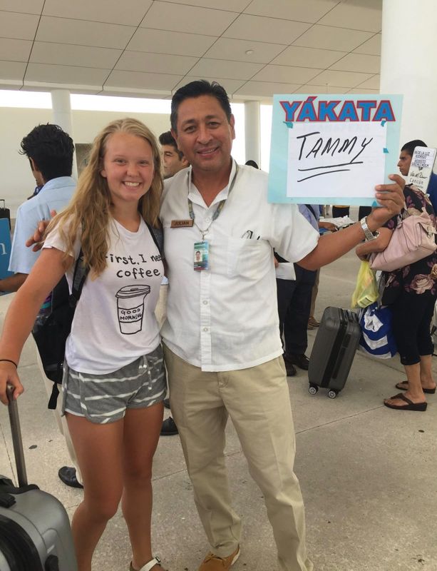 Julian welcoming a smiling traveller at Cancun airport with a Yakata name sign