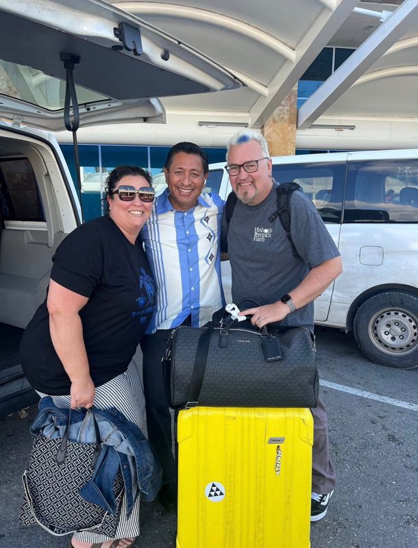 Julian with two happy guests and their luggage beside a white transfer van